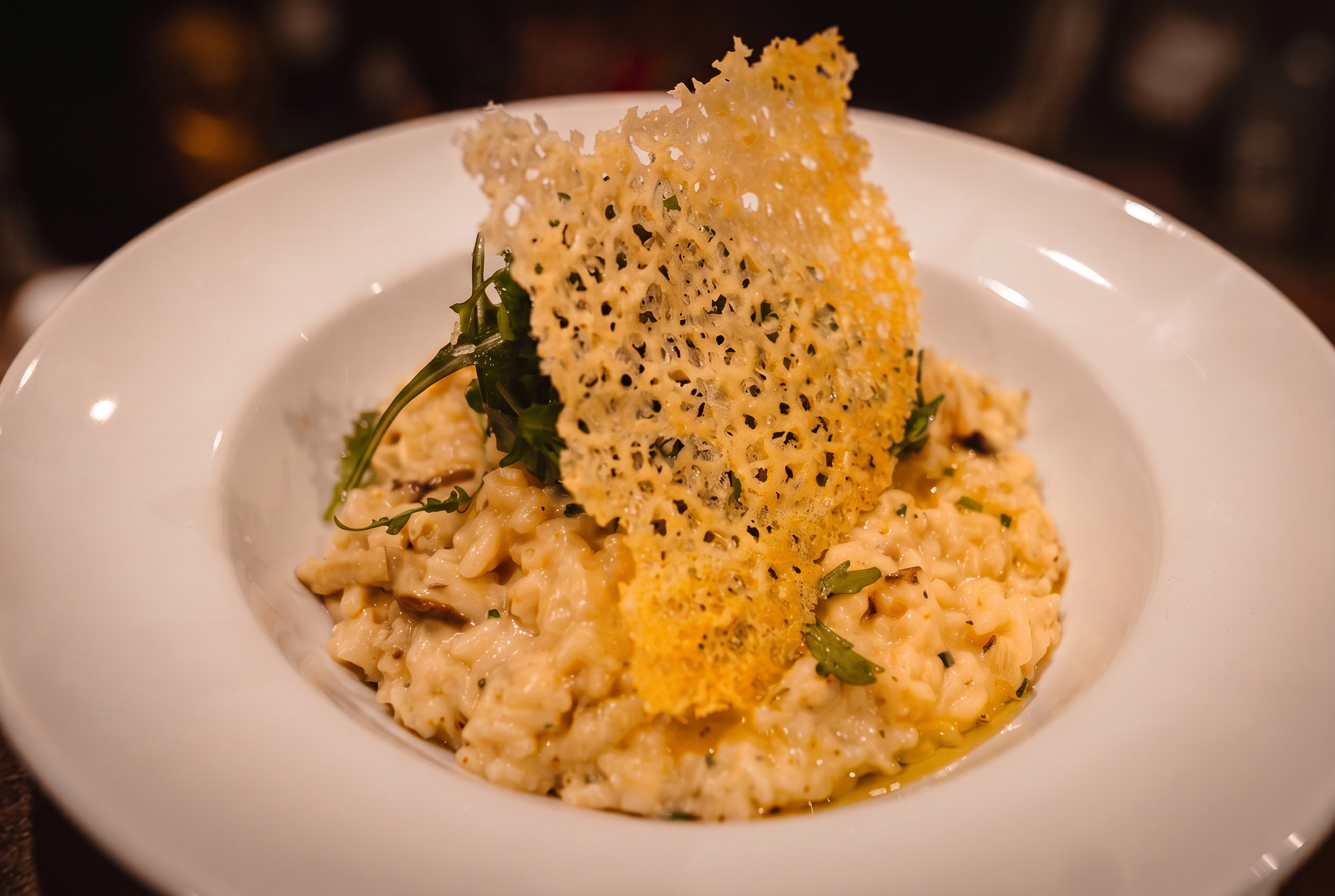 A server carries a beautifully plated risotto topped with a delicate parmesan crisp